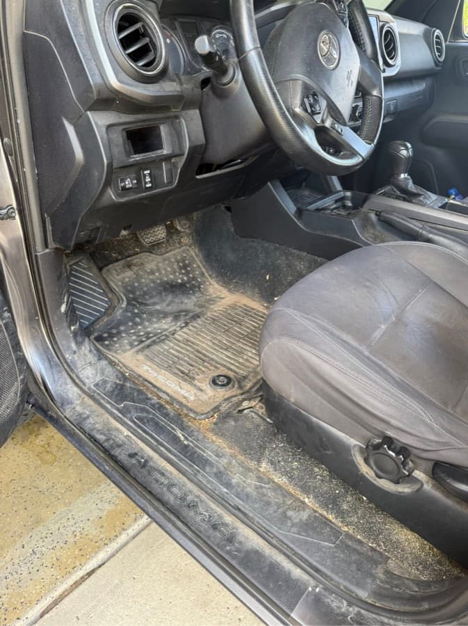 Toyota Tacoma driver-side floor mat coated in dirt and debris before a mobile interior detail